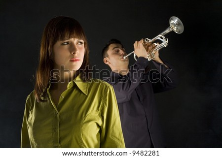 Trumpet man standing behind the woman. The woman looks thoughtful. Front view.