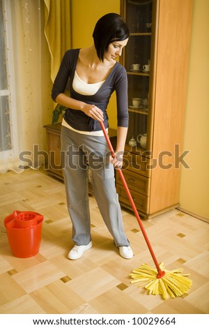 Young woman with the mop wipes the floor in room. Whole body. Front view.