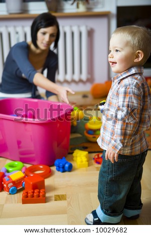 Young woman with baby boy during plaing. Woman stretches out for the toy. They are at container with toys. Focused on a boy.
