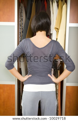 Young woman standing in front of wardrobe. She thinking what get dressed. She standing back to camera.