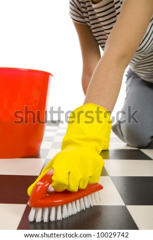 Young woman in yellow rubber gloves kneeling and scrubs the floor. Closeup on hand in glove with brush.