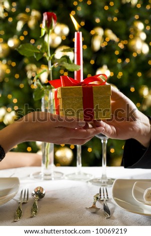 Couple during dinner party. They giving each other a present. Close up on hands with present.