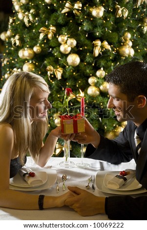 Couple at restaurant on dinner party. They giving each other a present.