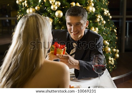 Couple at restaurant on dinner party. They giving each other a present. Focused on him.