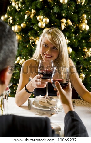 Couple at restaurant on dinner party. They're looking at each other and raise a toast. Focused on her.