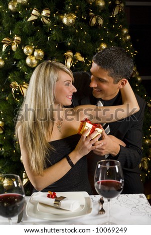 Couple at restaurant on dinner party. They giving each other a present. Front view.