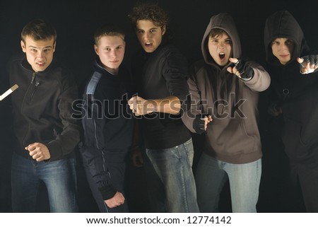 Group of screaming hooligans. They are looking at camera and standing in dark place. Two of them are pointing at camera. Front view