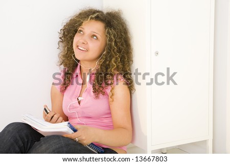 Young female student sitting and leaning for shool locker. She\'s listening to music by headset.