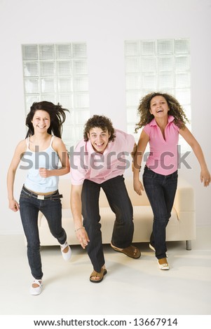 Three friends stood up from couch and started run. They\'re smiling and  looking at camera. Front view.
