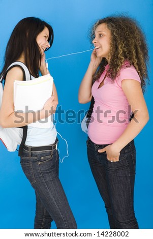 Young happy schoolgirls with backpack, holding notebook and listening to music by headset. Side view.