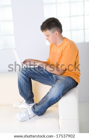 Young boy sitting on couch and typing on laptop.