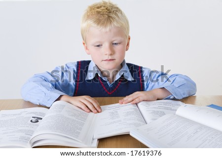 Young boy sitting at desk and reading books. Front view.