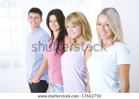 Group of smiling friends standing near window. They're looking at camera. Focused on two first girls.