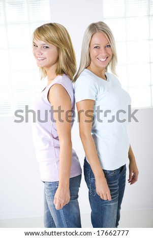 Two smiling girl standing back to back and looking at camera.