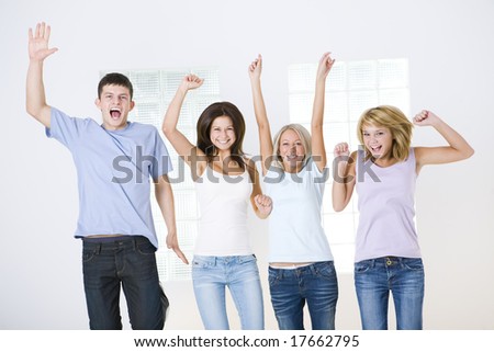 Group of young happy friends with upraised hands. They're looking at camera. Front view.