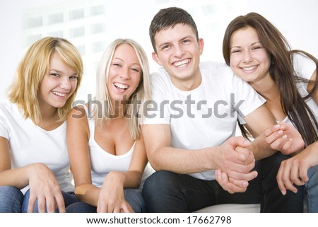 Group of young smiling friends sitting on a couch and looking at camera. Front view.