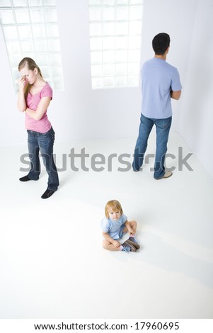 Young parents standing back to back. Theirs daughter sitting on the floor and looking at camera. High angle view.