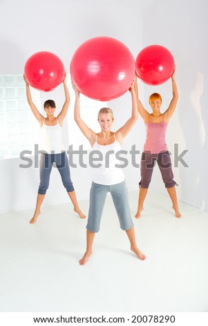 Group of women doing fitness exercise with big ball. They're looking at camera. Front view.