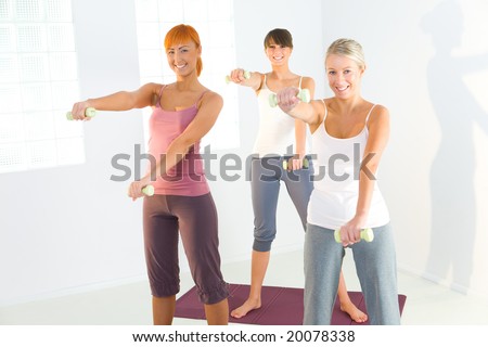 Group of women doing fitness exercise with dumbbells on mat. They\'re looking at camera.