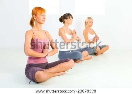Three women sitting cross-legged on the floor and meditate. They have closed eyes.