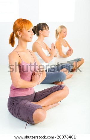 Three women sitting cross-legged on the floor and meditate. They have closed eyes.