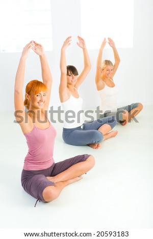 Three women sitting cross-legged on the floor with hands raised up. They\'re smiling looking at camera. Front view.
