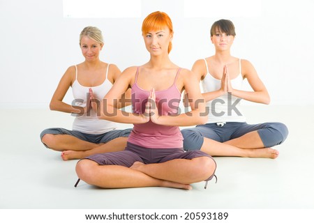 Three women sitting cross-legged on the floor and meditate.  Front view.