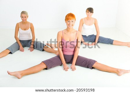 Group of women sitting on the floor and doing fitness exercise. They\'re looking at camera. Front view.