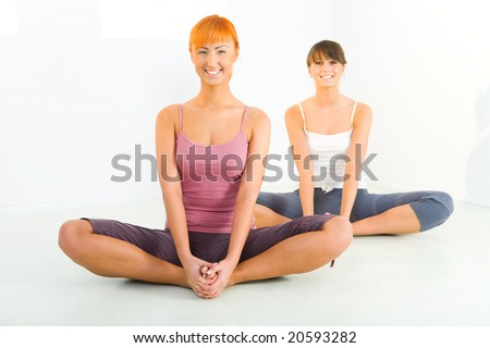 Three women sitting cross-legged on the floor. They\'re smiling looking at camera. Front view.