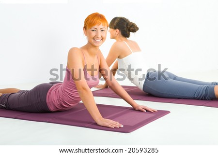 Two women doing fitness exercise on mat. They're looking at camera.
