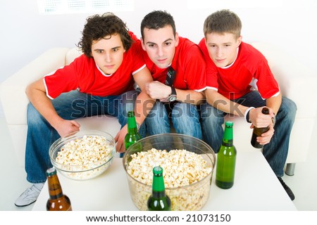 Three young men sitting on couch and watching sport on TV. Front view.