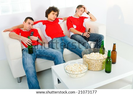 Three bored men sitting on couch and watching TV.