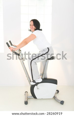 Elder woman exercising on bike. She\'s smiling and looking at camera. Side view.