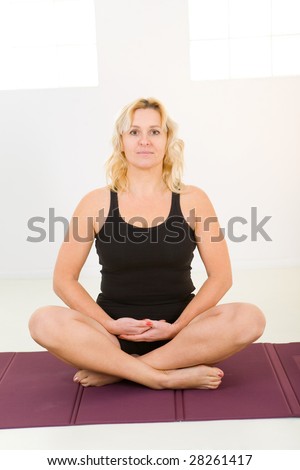 Woman sitting cross-legged on mat. She\'s smiling and looking at camera. Front view.