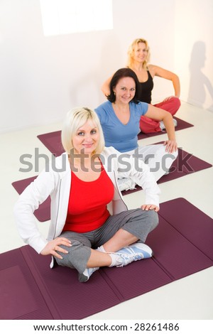 Elder women sitting cross-legged on mat and doing exercices. They're looking at camera. High angle view