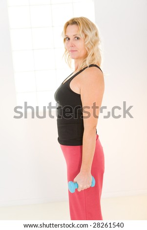 Elder woman exercising with dumbbell. She\'s looking at camera. Side view.