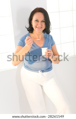 Elder woman eating yoghurt. She\'s smiling and looking at camera.