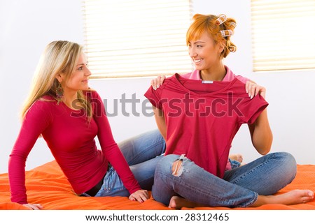 Two girls sitting on bed. Girls with hair rollers on head showing T-shirt.