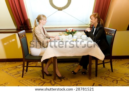 Two happy women sitting at table in restaurant. They\'re talking.