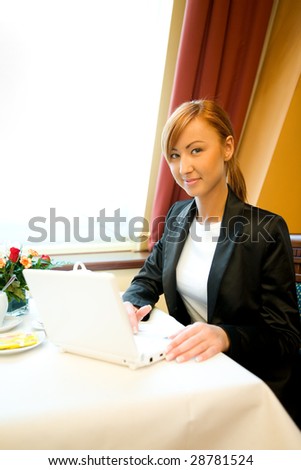 Young woman sitting in restaurant and doing something on laptop.
