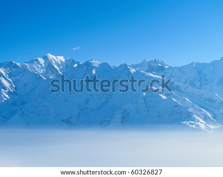 Snow covered mountains rise above morning mist on sunny day
