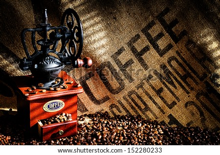 Cup of steaming hot coffee with coffee beans, coffee grinder, and coffee beans bag in background.