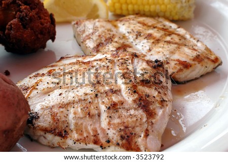 Grilled amberjack with corn, hush puppies, and lemon slice.