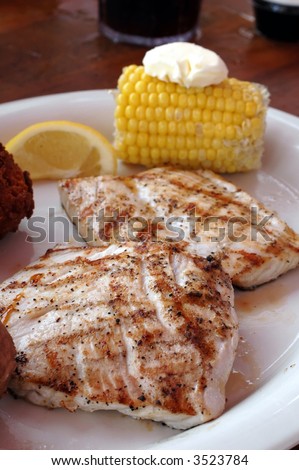 Grilled amberjack with corn on the cob, hush puppies, and lemon slice.