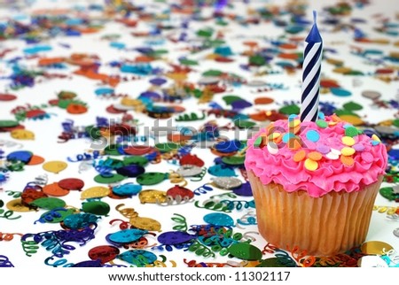 Celebration cupcake with candle and sprinkles with confetti in background.