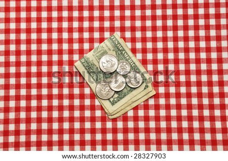 Tip left on restaurant table.  Bills and coins on red gingham tablecloth.