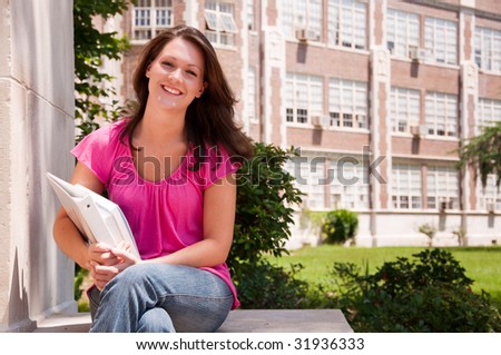 Female college student seated with books in hand at school.