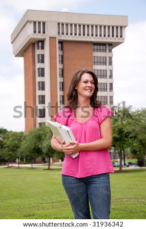 Female college student standing in front of school with books in hand.