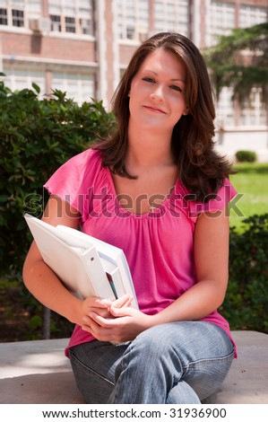 Female college student sitting with books in hand at school.
