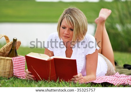 Young blond woman on picnic with book, picnic basket and wine.  Gingham blanket and napkin.